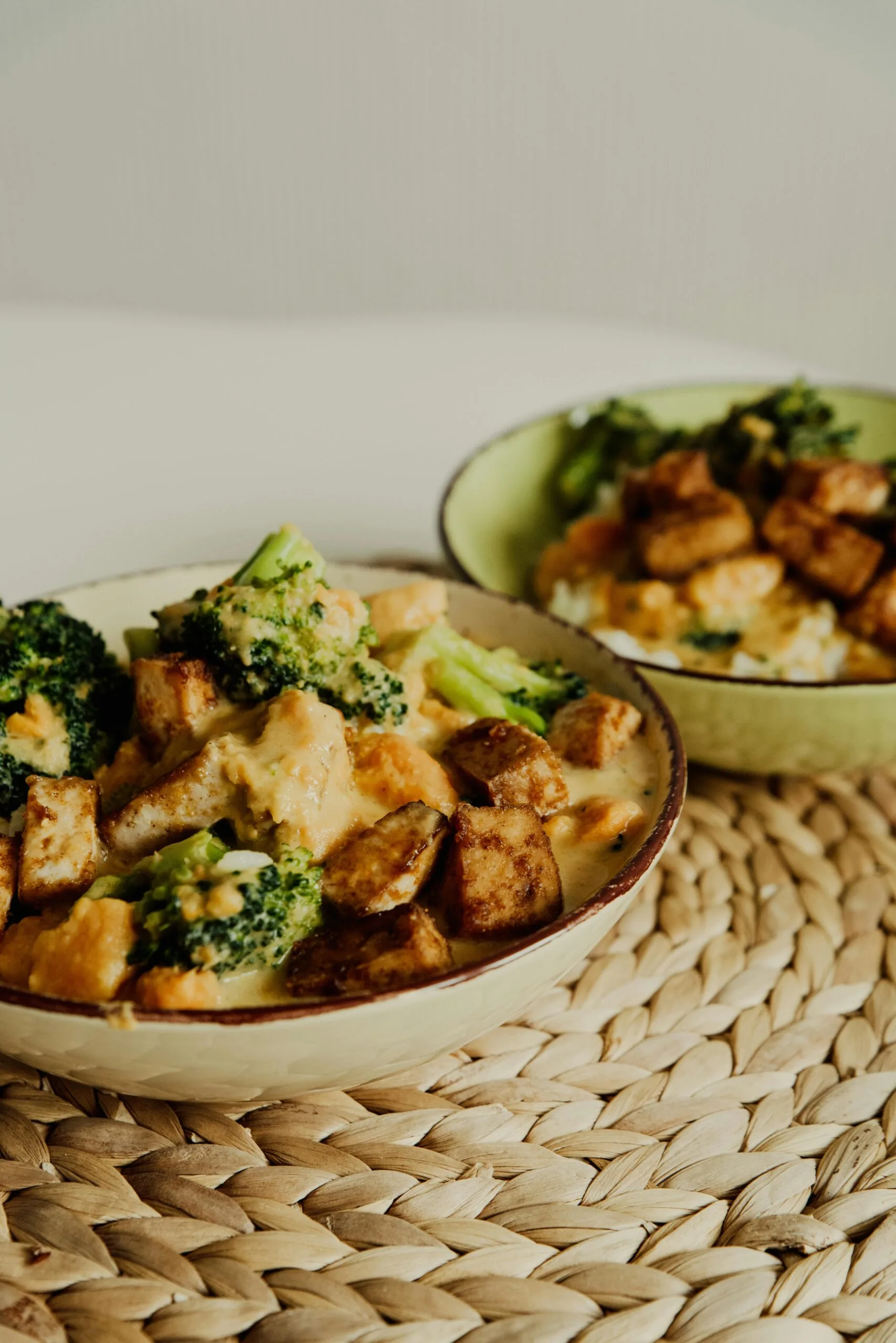 A mouthwatering bowl of vegan curry featuring tofu and broccoli, resting on a woven placemat.